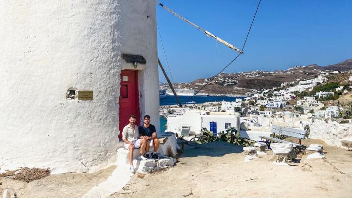 Gay couple sitting by the iconic windmill on Mykonos island.